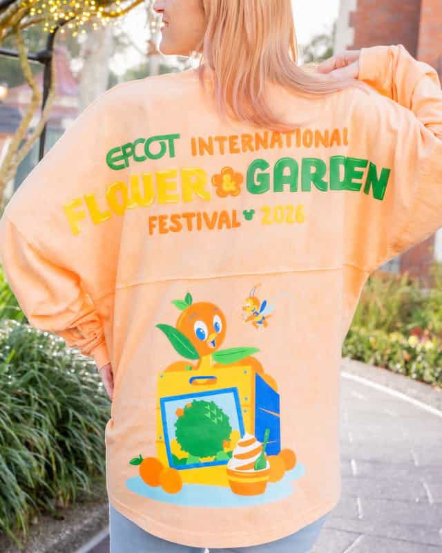 Woman wearing Disney Flower & Garden Festival sweatshirt with colorful Disney-themed design.