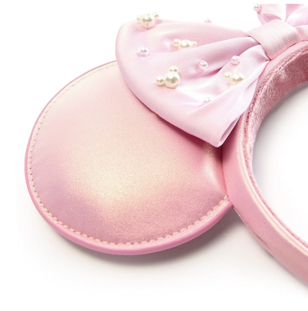 Pink Minnie Mouse ears headband with pearl accents and satin bow for Disney fans.