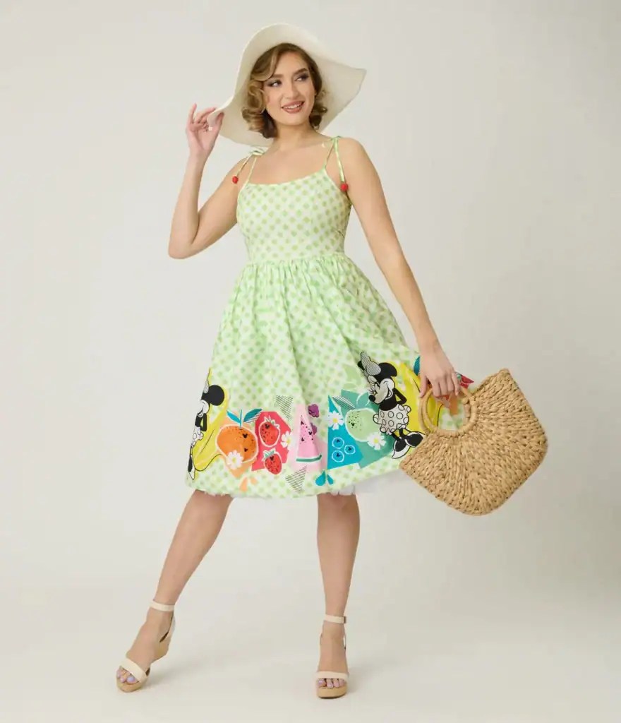 Woman in green polka dot Disney-themed dress with Mickey Mouse print and straw bag.