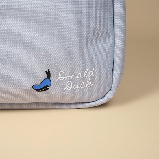 Close-up of a light blue Donald Duck-themed backpack with embroidered logo.