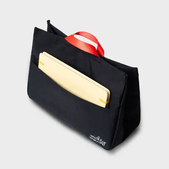 Black Mickey Mouse tote bag with red handle and yellow notebook inside.