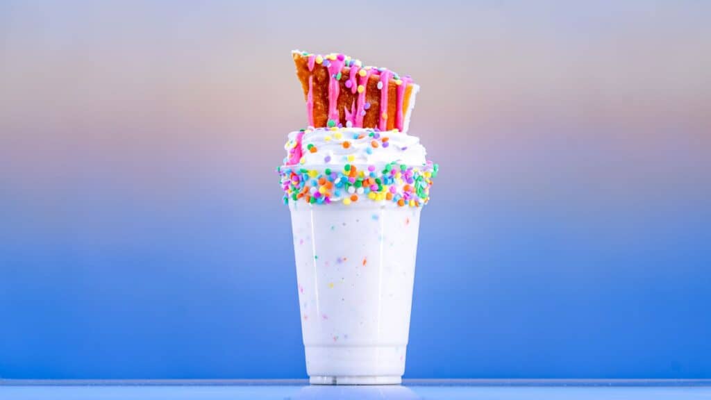 Colorful birthday cake milkshake with sprinkles in a glass.