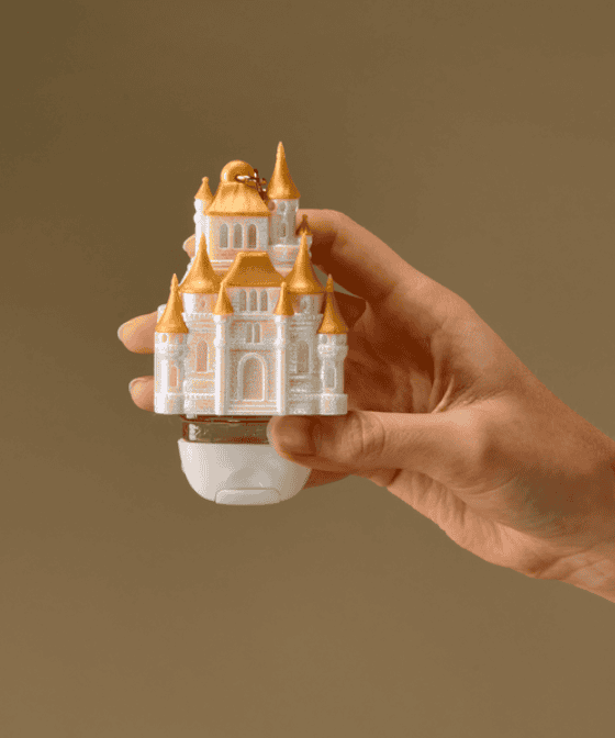 Hand holding a miniature Disney castle toy with gold turrets.