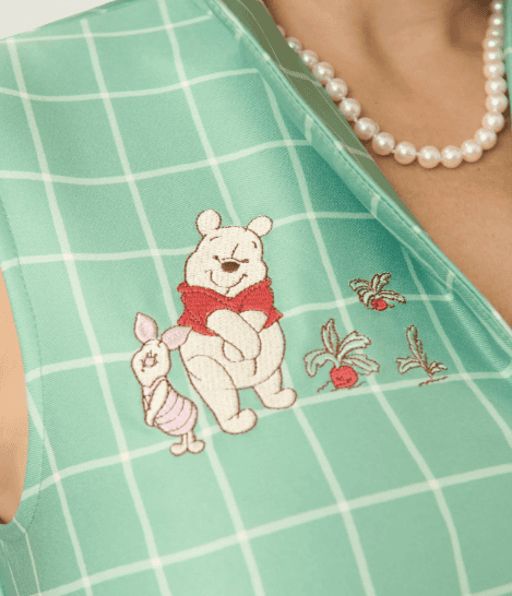 Winnie the Pooh and Piglet embroidery on green checkered fabric, with floral details.
