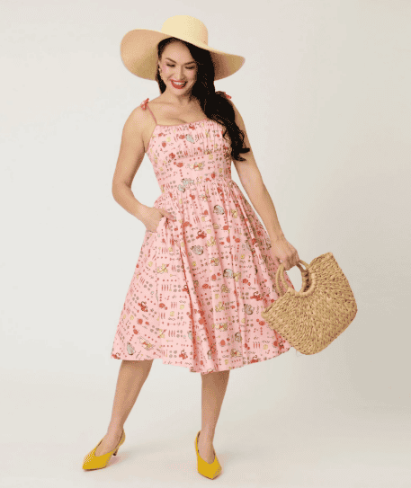 Stylish summer dress featuring a pink Disney-themed pattern, paired with a wide-brim straw hat and a.