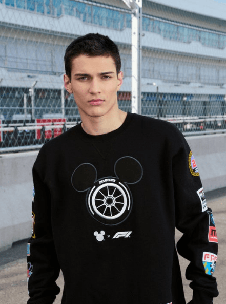 Young man in black Disney racing sweatshirt with F1 and Mickey Mouse logos.
