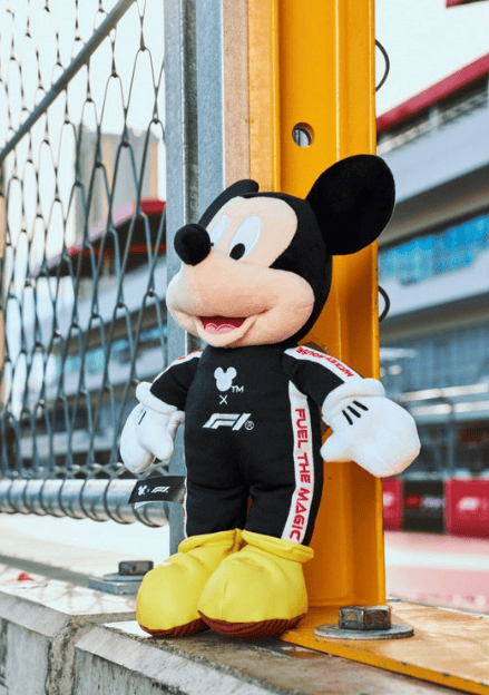 Mickey Mouse plush toy dressed in racing gear at a motorsport event.