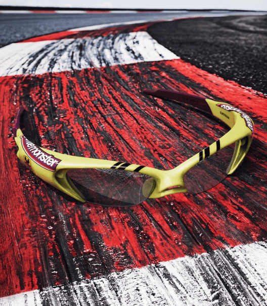 Yellow racing sunglasses on a red and black textured track surface.