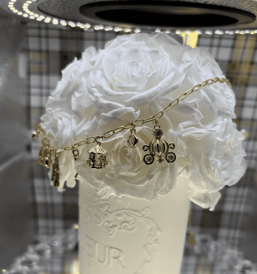 Gold Disney charm bracelet with Mickey Mouse and castle charms on white roses.