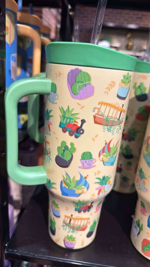 Colorful Disney-themed plant mug with green handle and lid.
