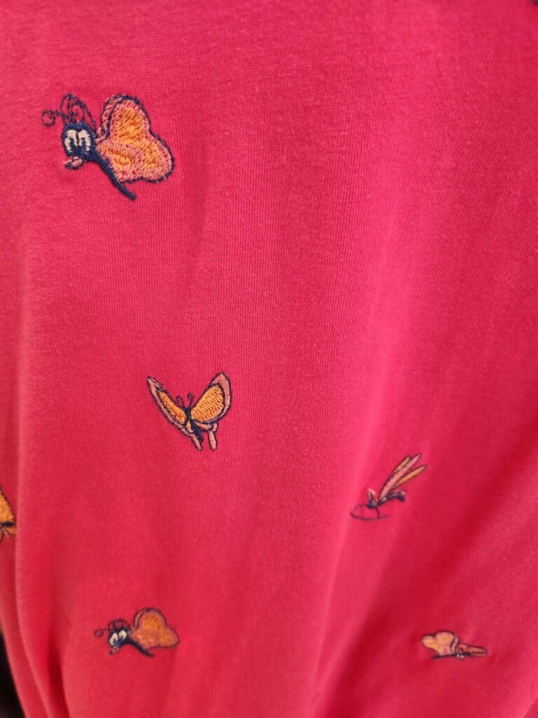 Pink fabric with embroidered butterflies and insects, inspired by Disney fashion designs.
