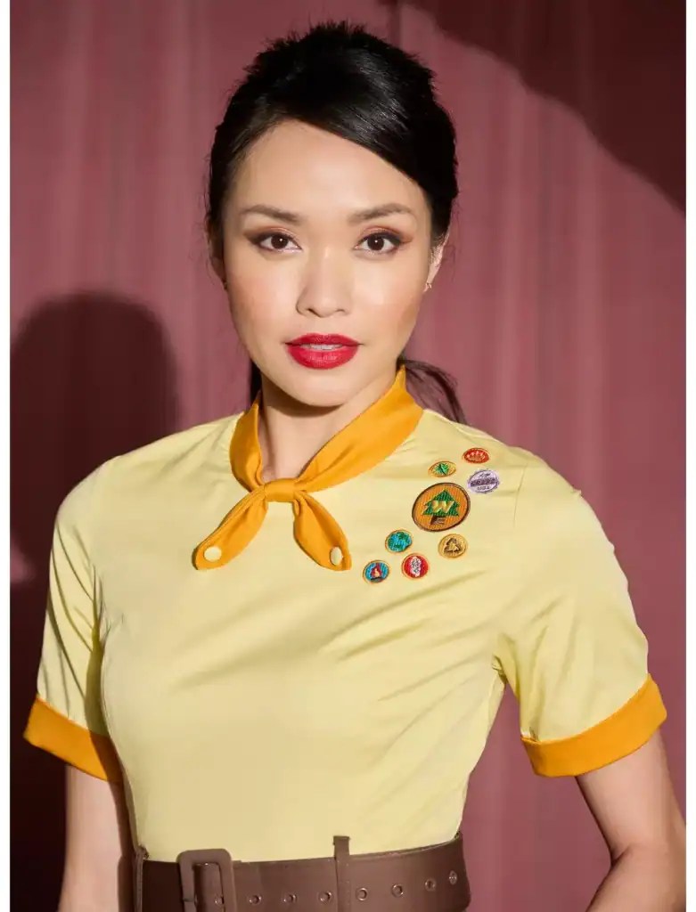 Girl Scout wearing uniform with badges and yellow neckerchief, smiling confidently.