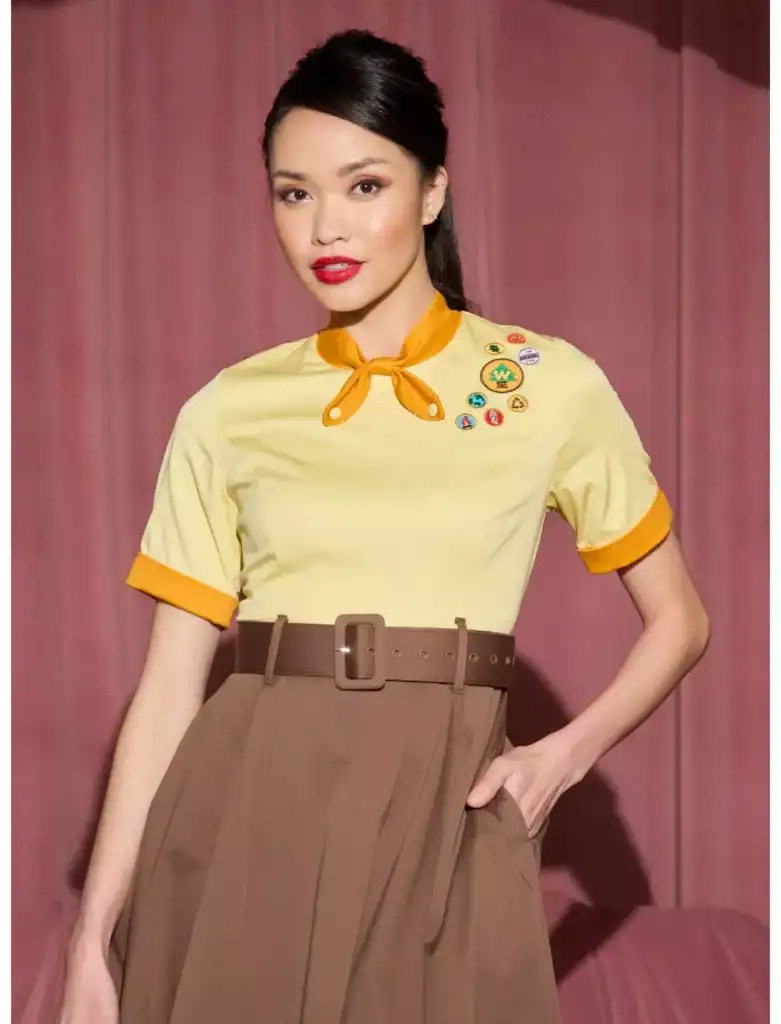 Woman in vintage-inspired yellow top with badges and brown skirt.