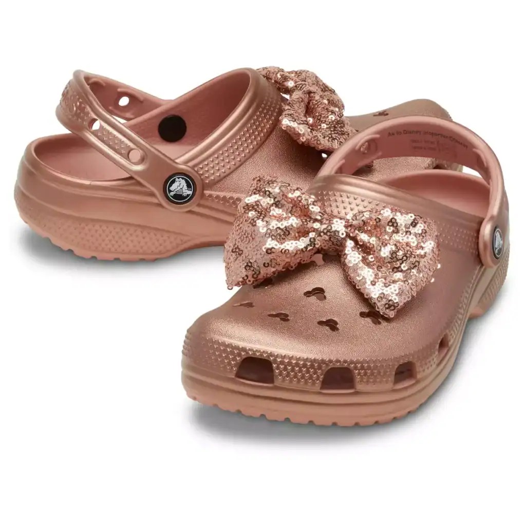 Pink Disney Crocs with sequin bow, heart cutouts, and adjustable strap.