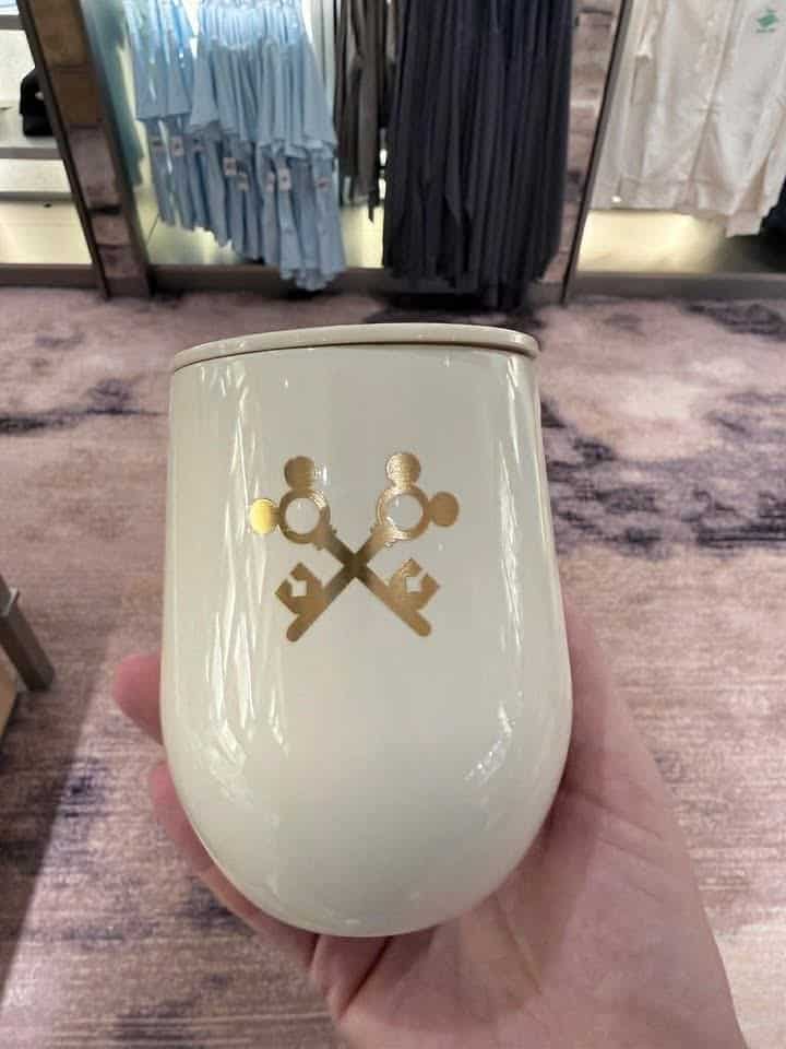 White ceramic mug featuring a gold key design, held in a retail store setting.