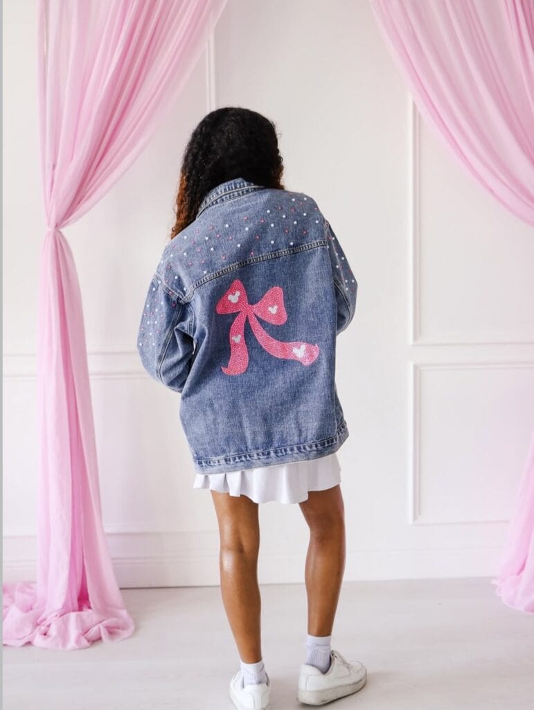 Trendy denim jacket with pink bow design and rhinestone details for Disney fashion fans.