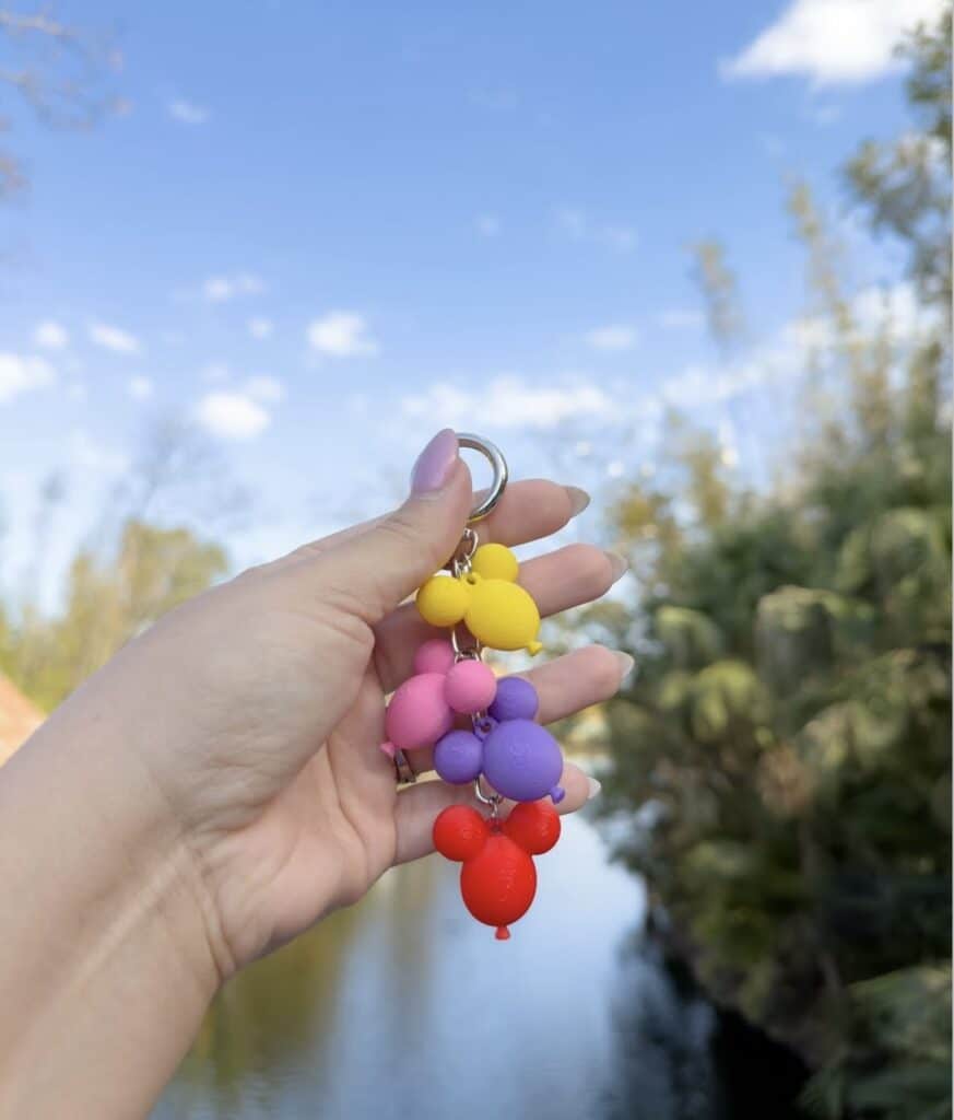 Hand holding a vibrant Mickey Mouse keychain outdoors against a blue sky.
