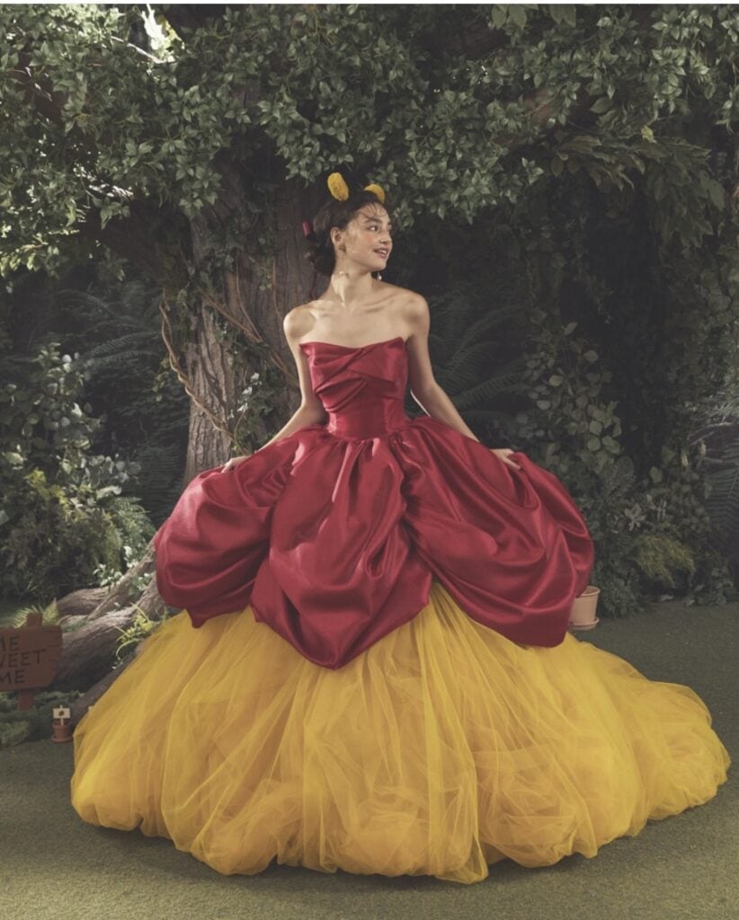 Woman in vibrant red and yellow Disney-inspired fairy tale gown outdoors.