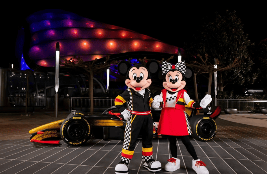 Mickey and Minnie Mouse in racing outfits at Disney theme park.