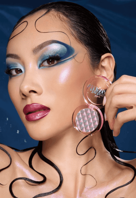 Woman with vibrant blue and purple makeup holding Disney-themed makeup products.