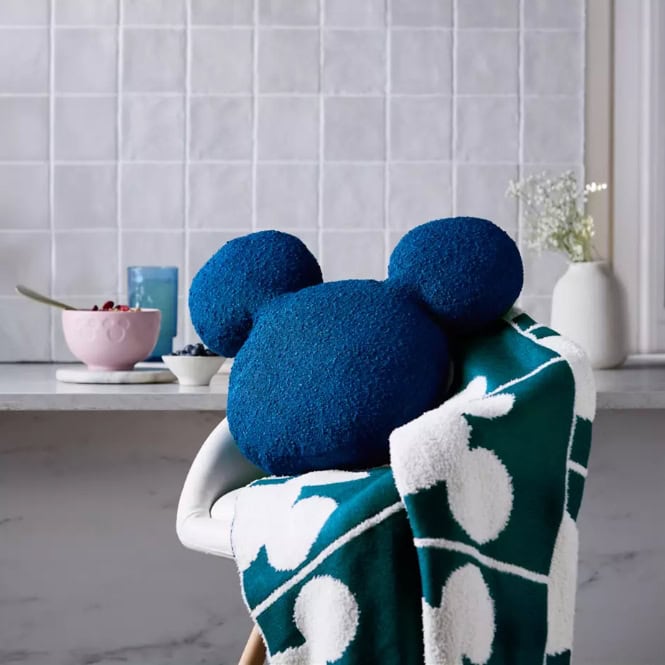 Blue Mickey Mouse plush toy with a Disney-themed blanket in a cozy home setting.