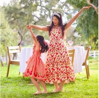 Young girl dancing with woman in a garden, wearing strawberry-themed dresses.