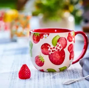 Red and green strawberry-themed Mickey Mouse mug on a table.
