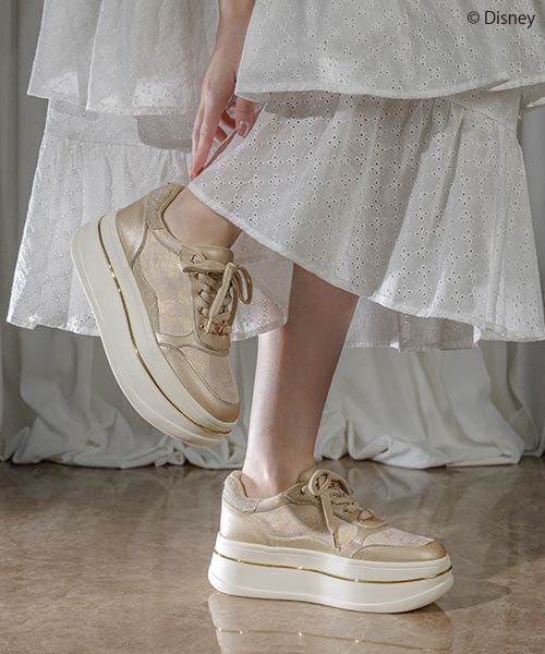 Woman wearing stylish gold platform sneakers with white dress.