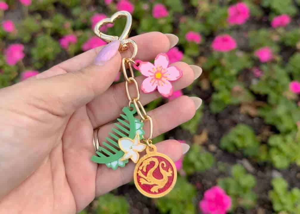 Disney-themed keychain with pink flower, leaf, and circular charm, held outdoors.