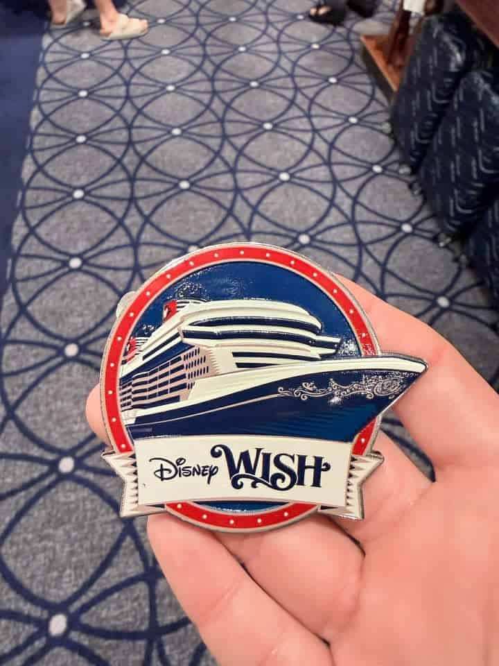 Disney Wish cruise badge held in hand with ship illustration and logo.