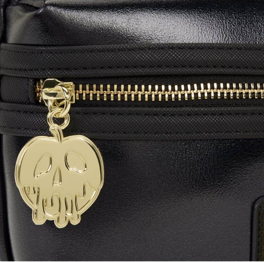 Gold skull bag charm hanging from a black bag with a gold zipper.