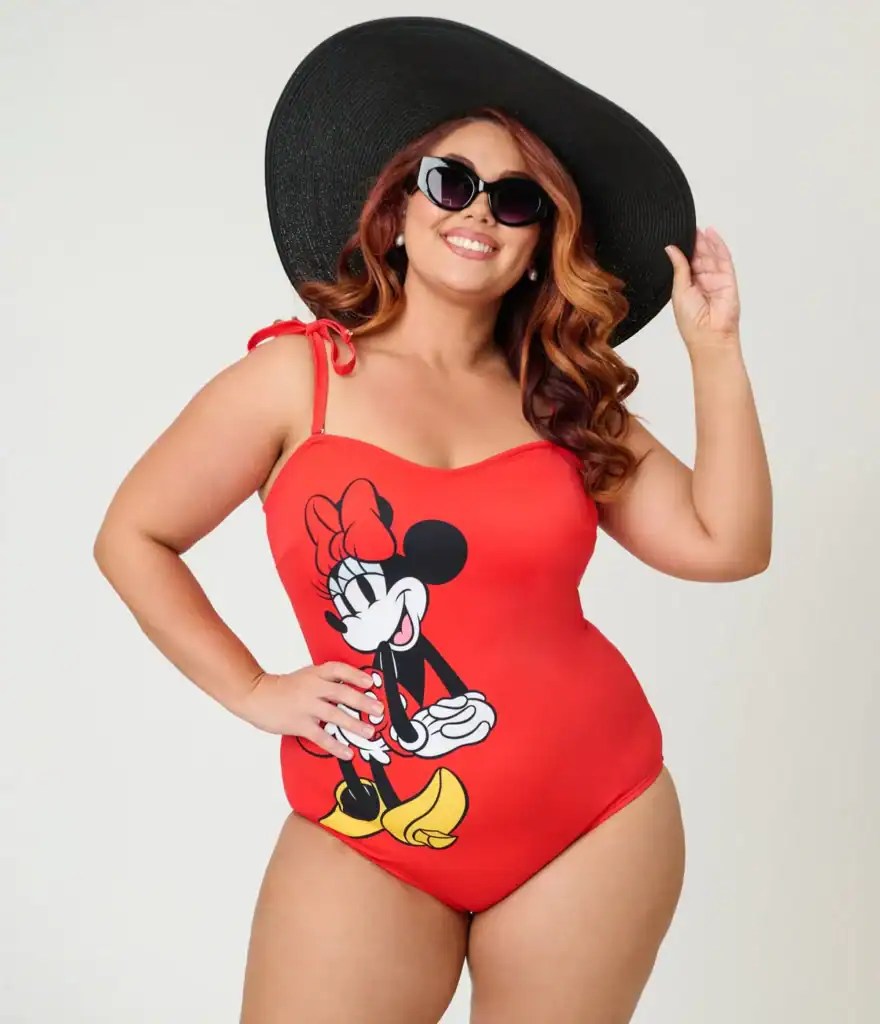 Woman in Minnie Mouse swimsuit with large sun hat and sunglasses.