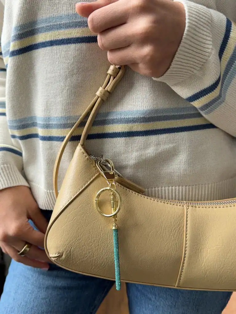 Stylish beige handbag featuring a turquoise keychain charm and gold hardware. Perfect for Disney-ins.