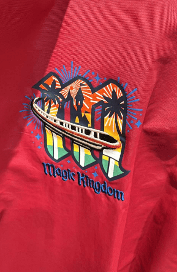 Colorful Disney Magic Kingdom logo with fireworks and castle on red fabric.
