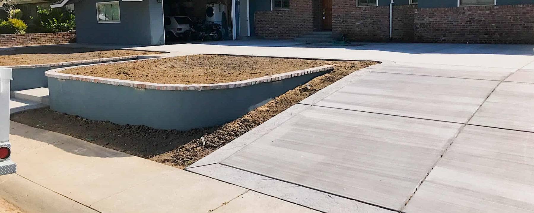 A new concrete driveway with an integrated raised planter bed borders a residence in Elk Grove