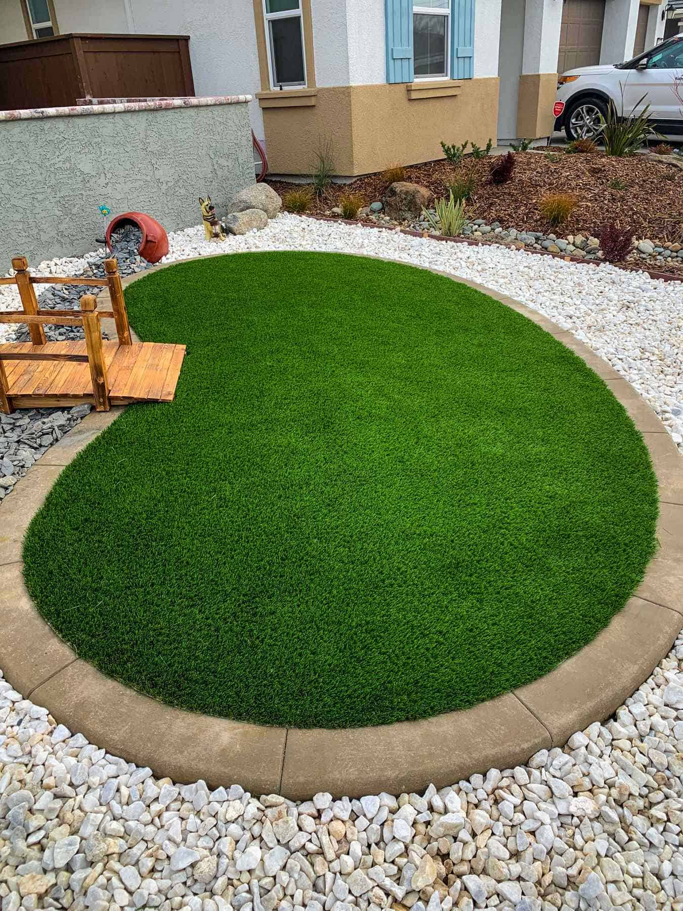 A neatly installed artificial turf lawn with decorative white rocks and concrete curbing in a front yard in Folsom