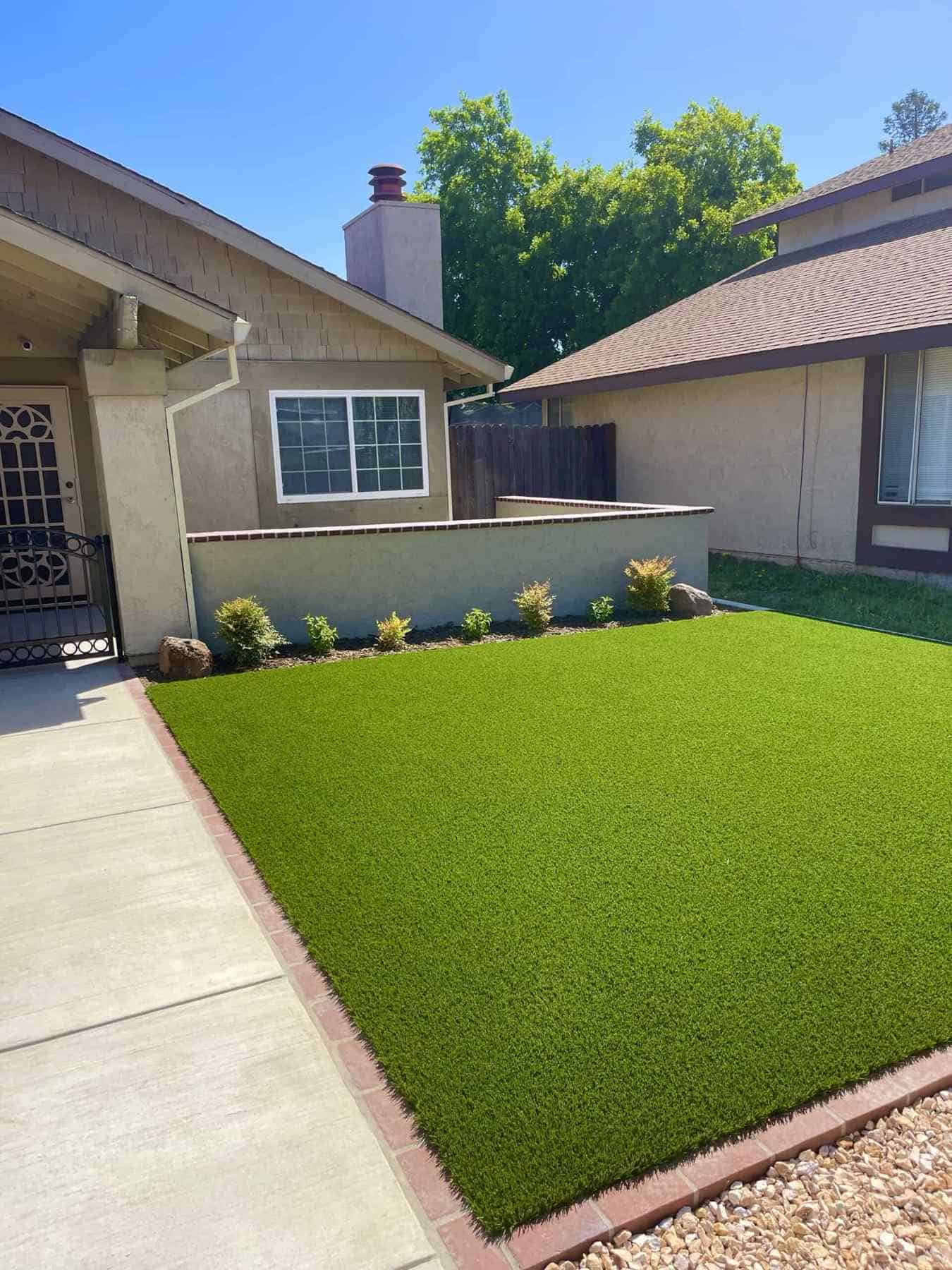 A beautifully installed artificial turf lawn with a red paver border and concrete walkway enhances a residential front yard in Lodi
