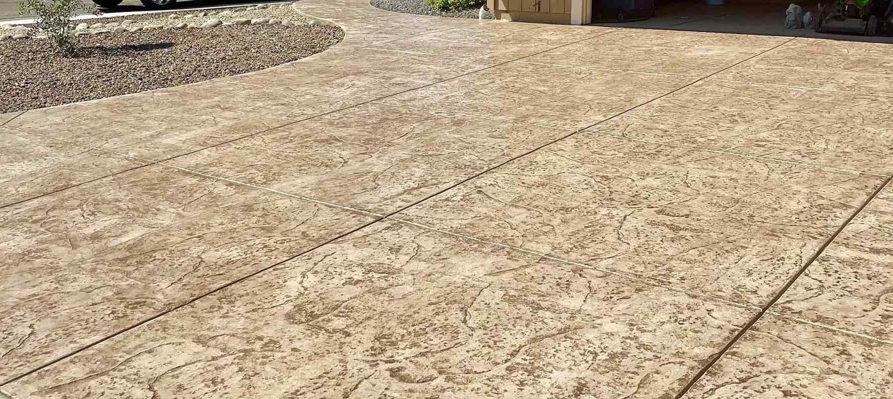 A tan stamped concrete driveway with a subtle textured pattern connects to a curved walkway in a residential front yard in SACRAMENTO