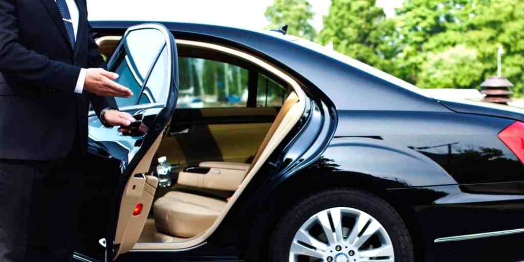 Luxury Mercedes sedan with open door showing beige interior, professional chauffeur in dark suit hol