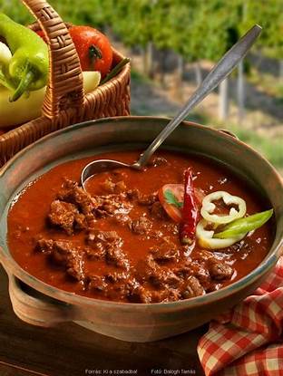Traditional Hungarian goulash stew in outdoor setting with fresh vegetables and picnic basket