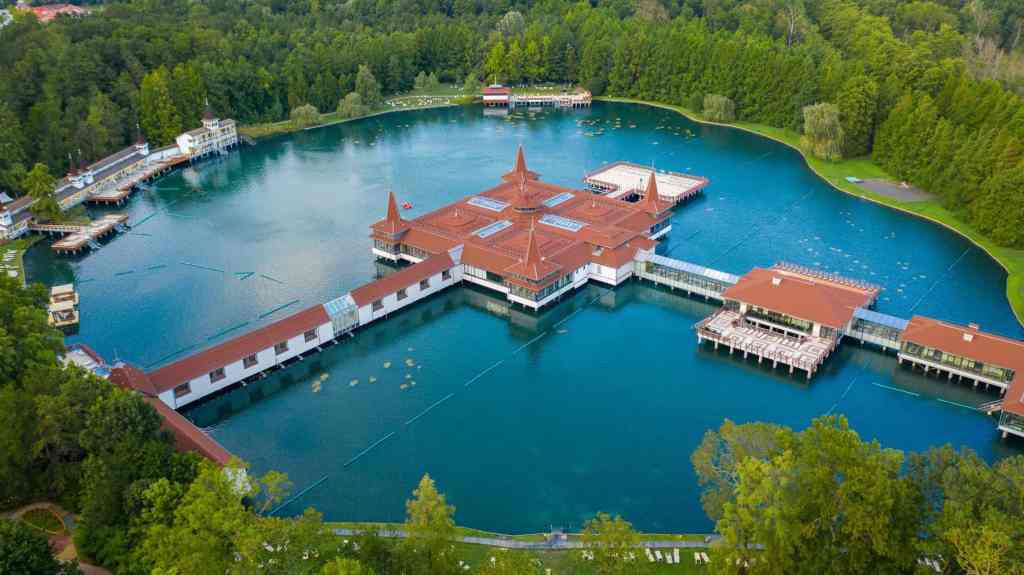 Aerial view of luxury lakeside resort in Hungary with turquoise water, red-roofed buildings, and den