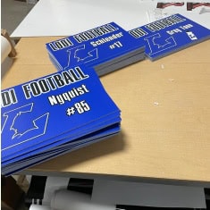 Stack of blue football program booklets with white text and graphics, designed for sports event promotion at I39 Supply Trailer Dealership.