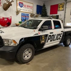 White police pickup truck with black police markings and badge, parked inside I39 Supply dealership, showcasing law enforcement vehicle inventory.