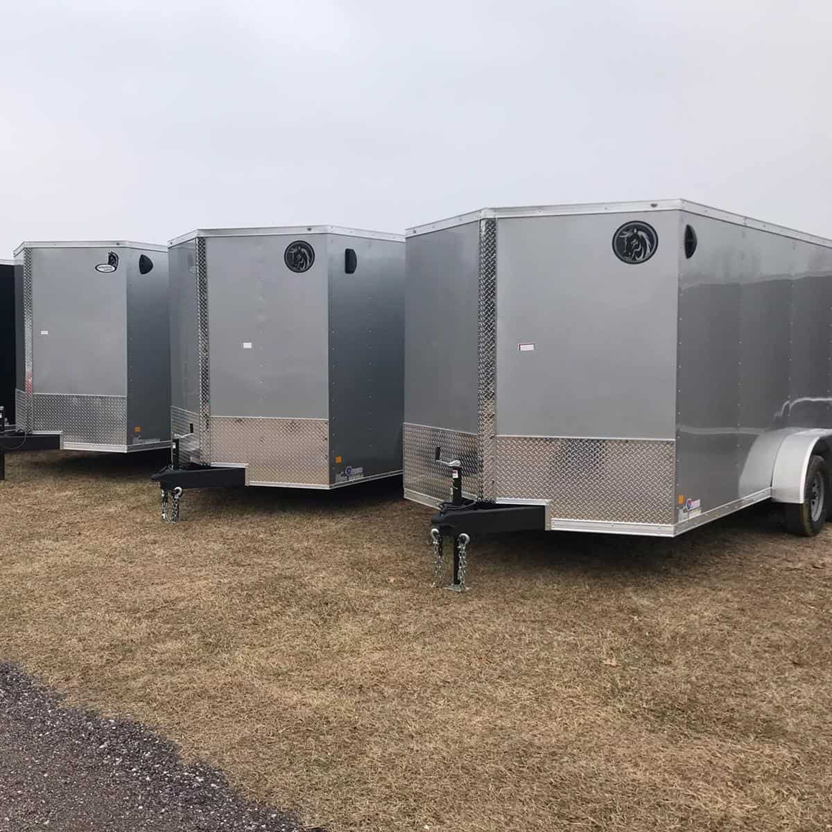 Multiple silver enclosed trailers parked on a grassy lot at I39 Supply trailer dealership, showcasing durable construction and versatile storage options.