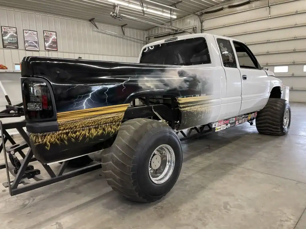 High-resolution image of a lifted, heavy-duty truck featuring a custom lightning storm and wheat field design, showcased inside a spacious dealership warehouse.