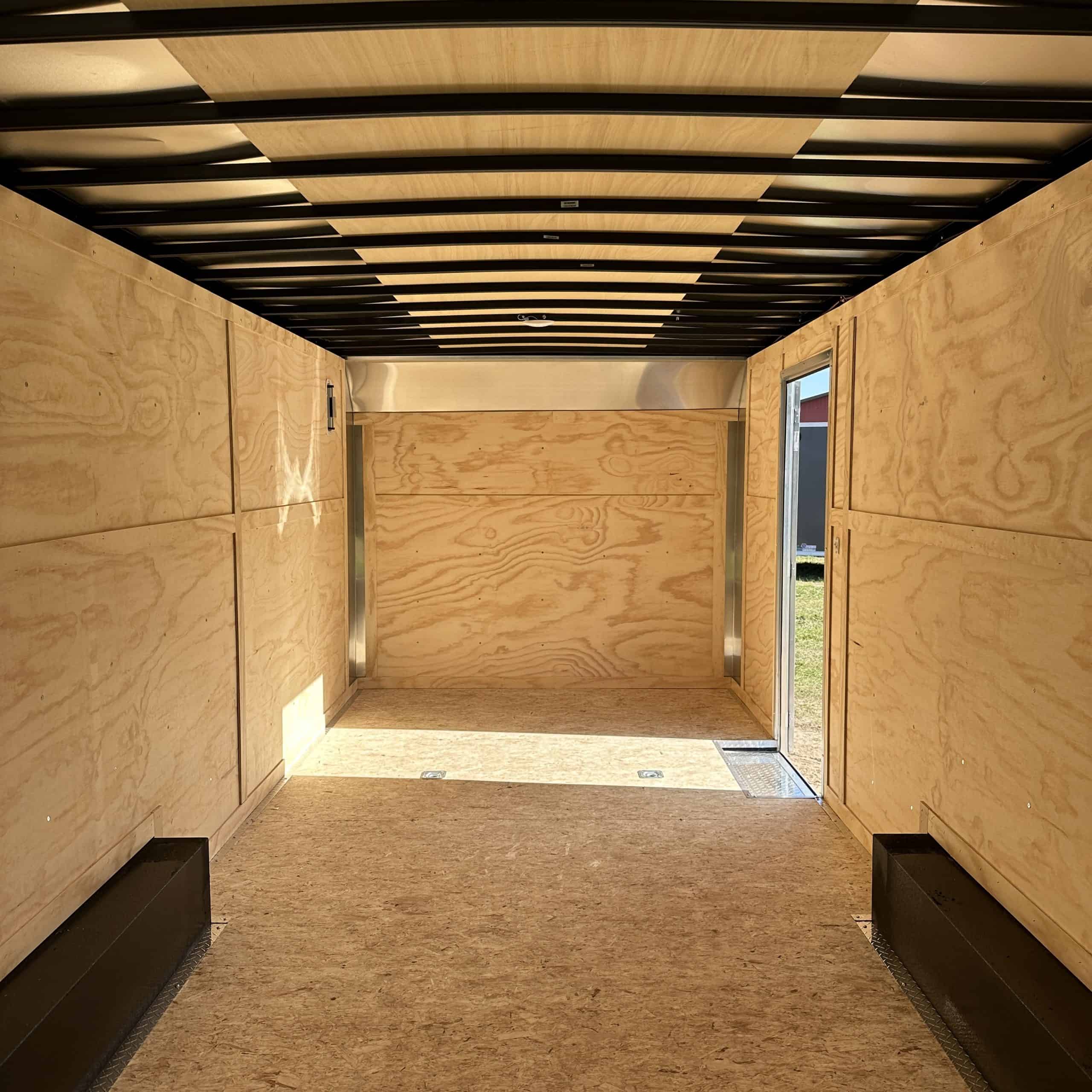 Interior view of a durable plywood cargo trailer with black wheel wells, ideal for transporting goods securely.