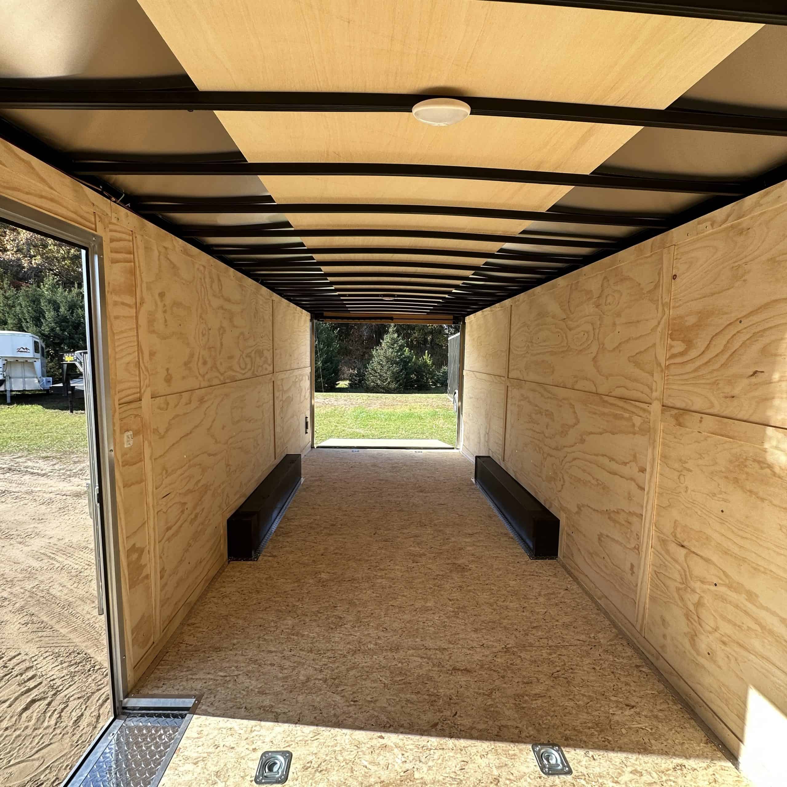 Interior view of a 8.5' x 24' Darkhorse tandem axle cargo trailer with 10k GVWR, showcasing durable plywood walls, black steel framing, and built-in benches for versatile storage and transport solutio.