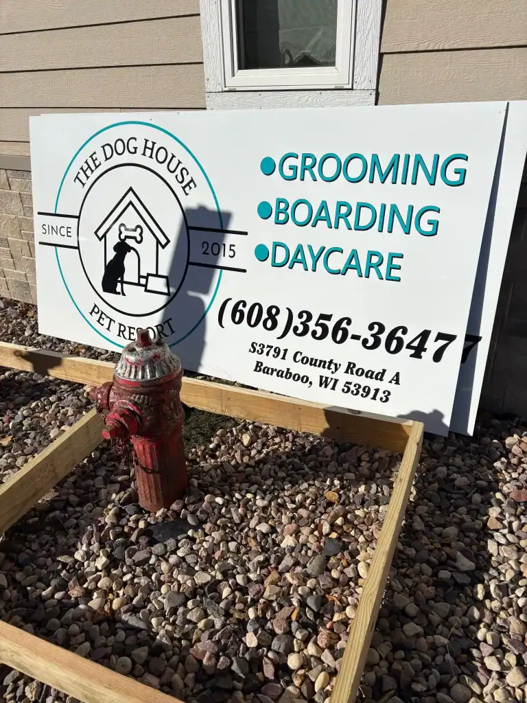 Dog House Pet Report sign with grooming, boarding, and daycare services, including contact number and address in Baraboo, WI.