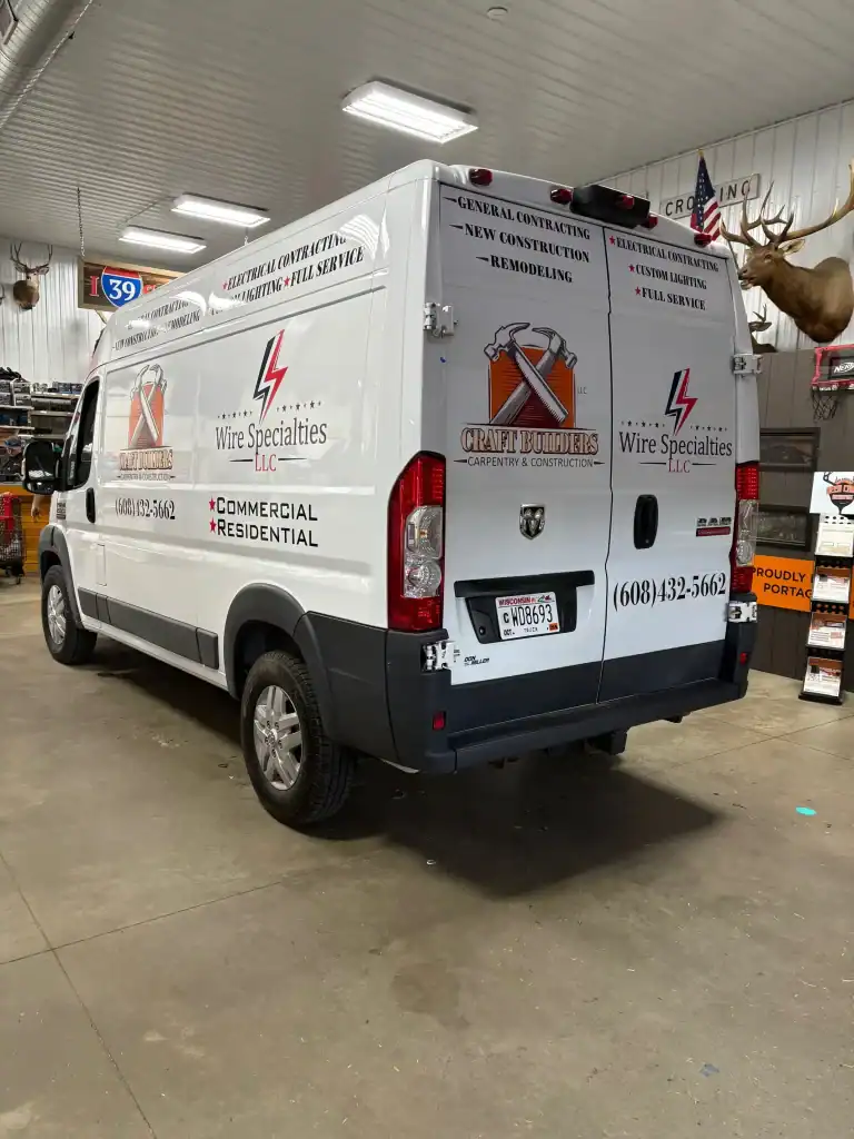 Service van for electrical wiring specialists featuring company logo and contact info, parked inside a dealership or workshop.