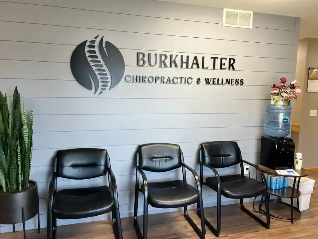 Modern chiropractic and wellness office reception area with three black chairs, a water cooler, and a potted plant, showcasing a professional healthcare environment.